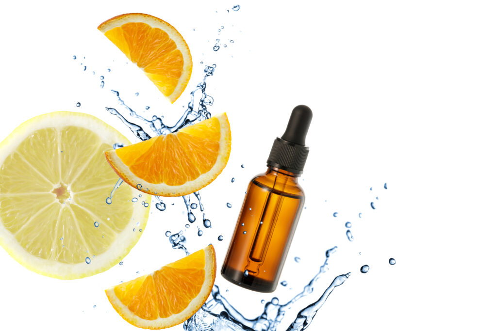 Image of amber colored serum dropper bottle splashing in water with slices of citrus fruit