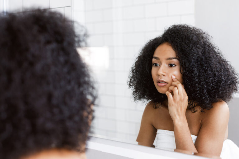 A young woman looking at mirror and examines her skin, touching
